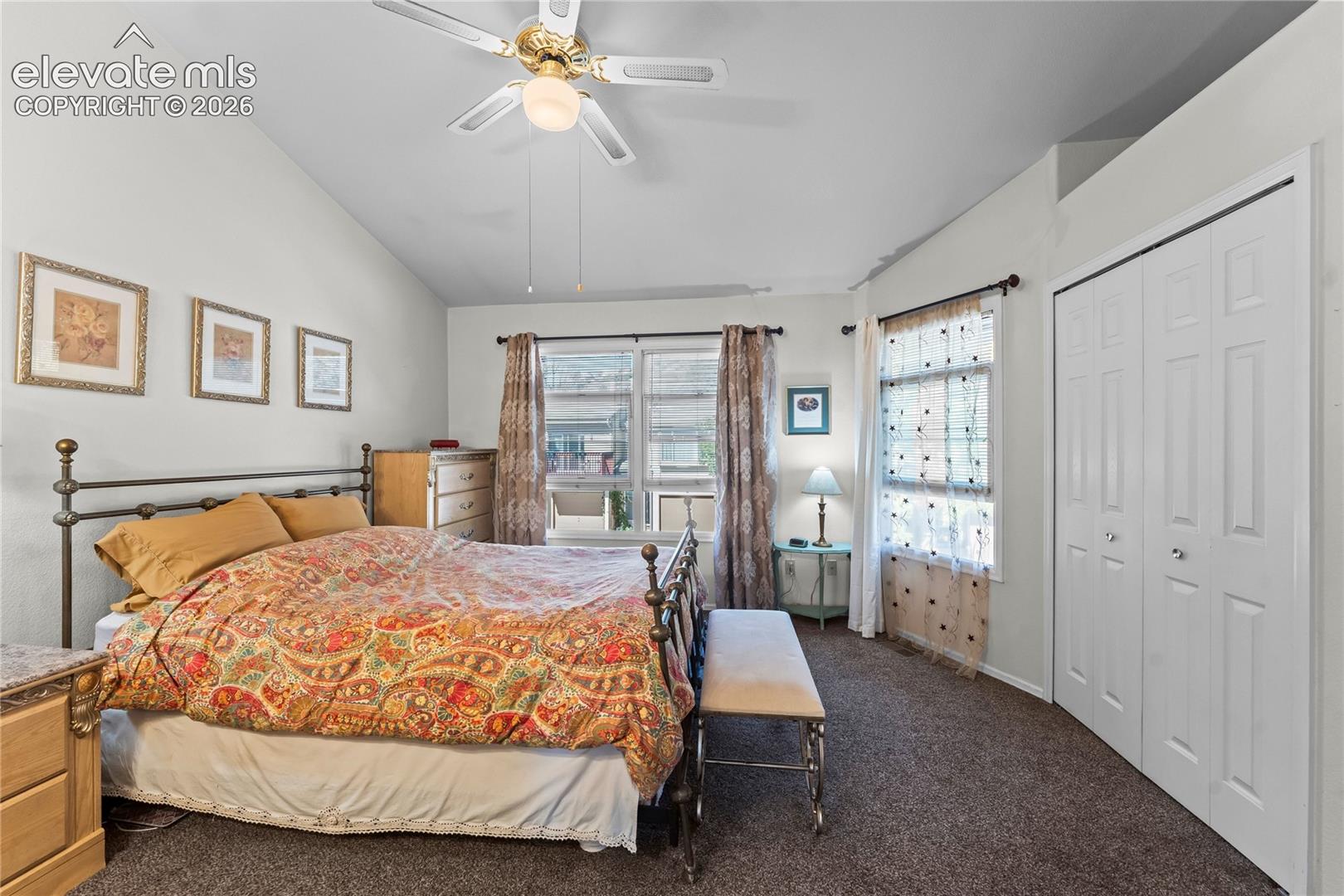 Vaulted ceiling with a ceiling fan, dual windows, and bifold closet doors