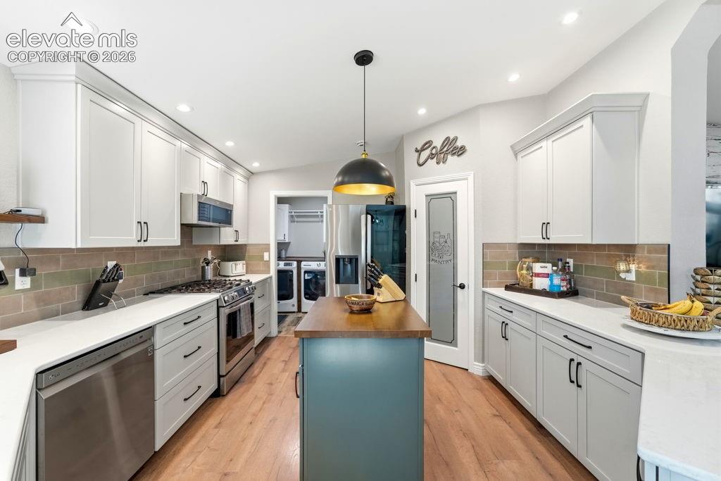 Light wood-finish flooring with white cabinetry, stainless steel appliances, and a central island with a wood-finish top