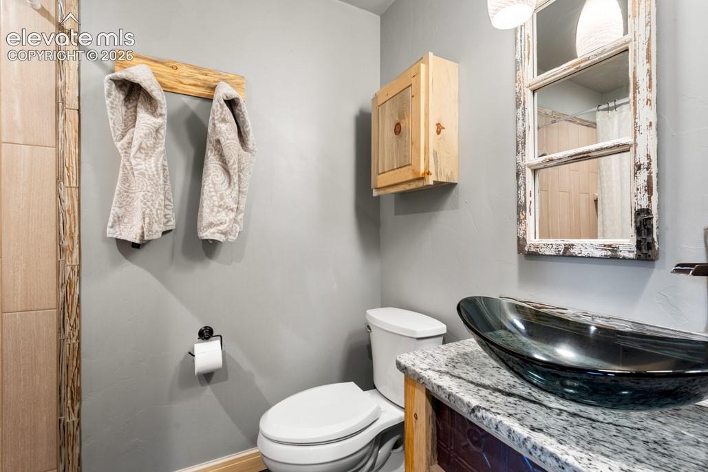 Vessel sink with a granite countertop, rustic vanity, and a wooden wall cabinet