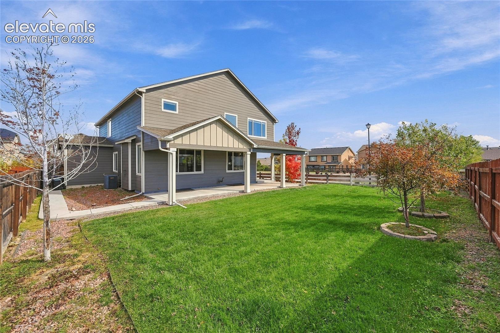Rear exterior featuring a covered patio, two-story horizontal siding, manicured lawn, and perimeter wood fencing