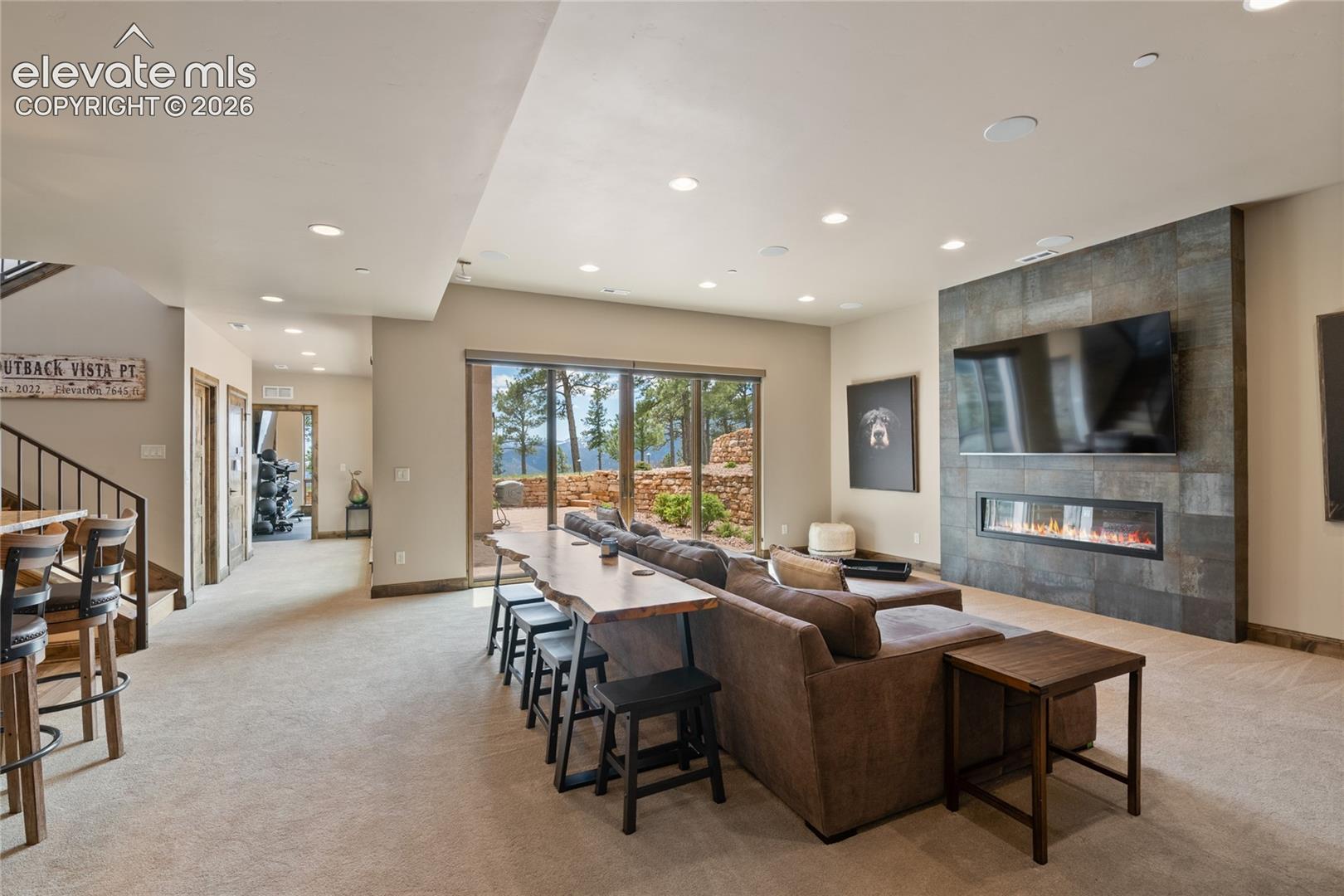 Made for hosting. Expansive lower-level family room with double-sided fireplace, live-edge bar seating, and walk-out to the backyard retreat.