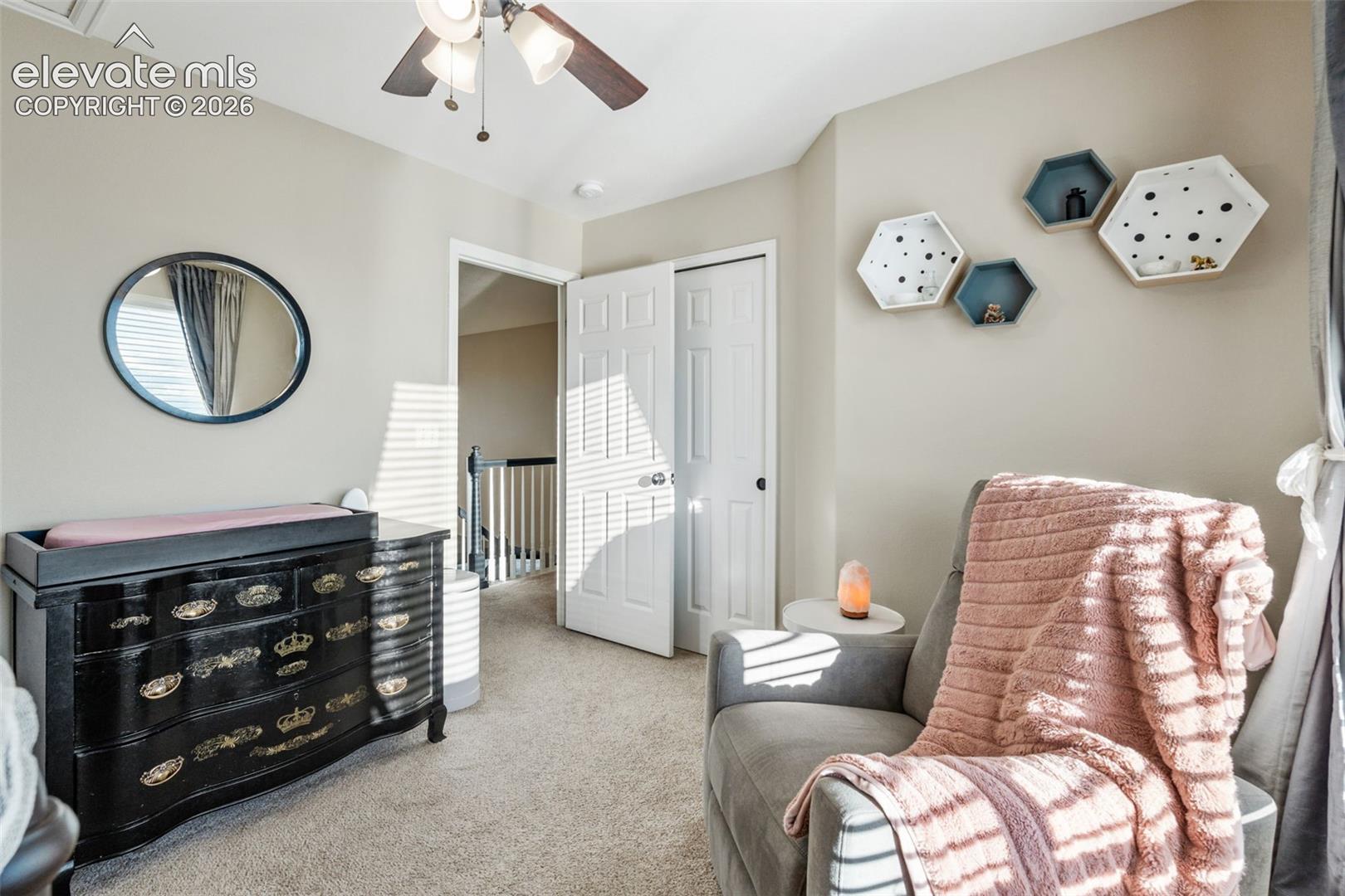 Neutral wall tones, wall-to-wall carpeting, dual-panel closet doors, ceiling fan with light fixture, and an oval wall mirror