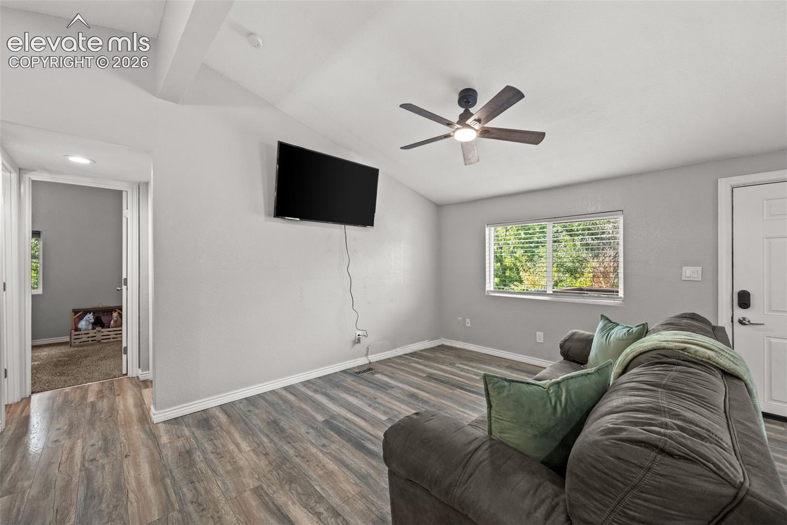Room featuring vaulted ceilings, wood-finish flooring, a ceiling fan with integrated lighting, and a single-hung window