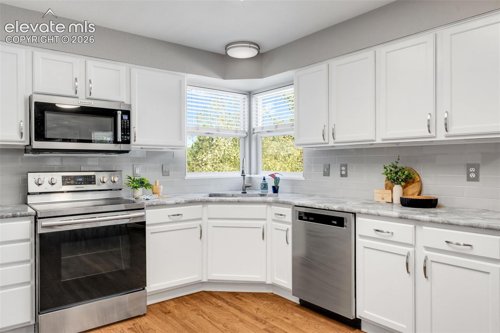 Kitchen featuring white cabinetry, stone-finish countertops, stainless steel appliances, a tile backsplash, and wood-finish flooring