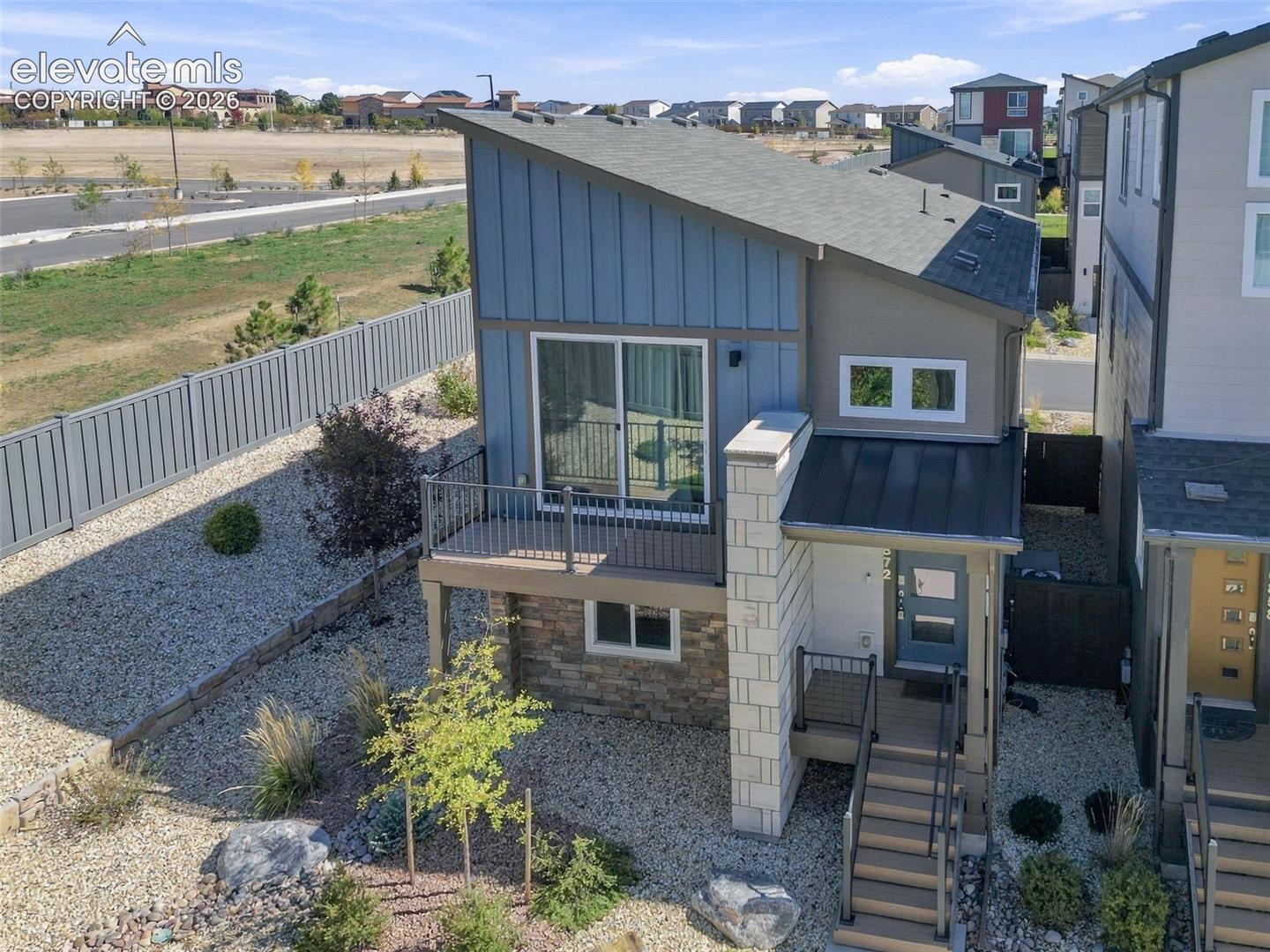 Contemporary exterior featuring a shed roofline, vertical board-and-batten siding, stone veneer accents, an elevated balcony with metal railing, and a covered entry staircase