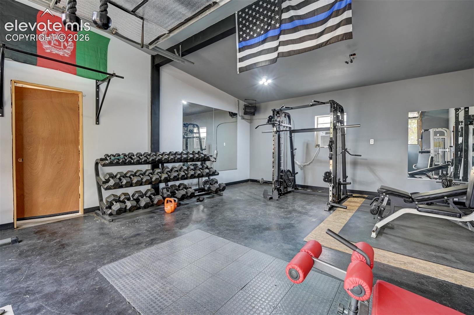 Dedicated fitness area with concrete flooring, wall-mounted mirrors, and track lighting