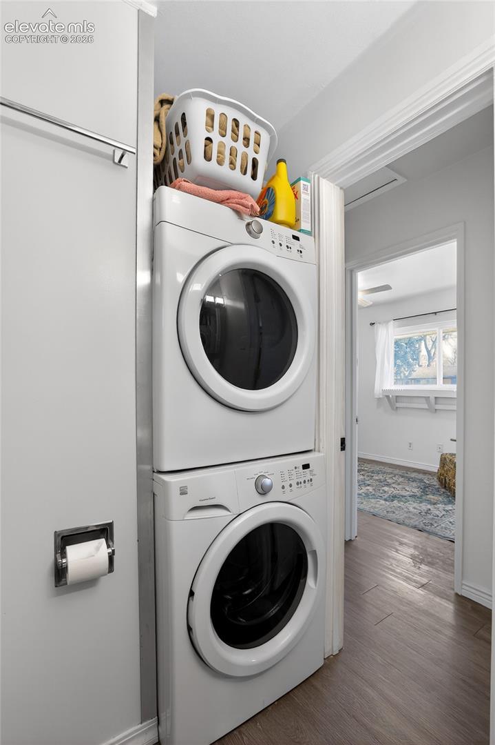 Dedicated laundry area featuring stacked appliances and wood-finish flooring