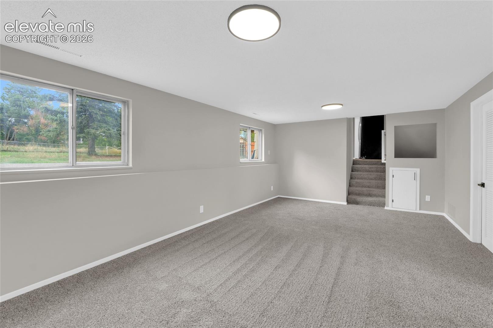 Recessed windows with outdoor scenery, light gray walls, gray carpet flooring, and flush-mount ceiling lighting