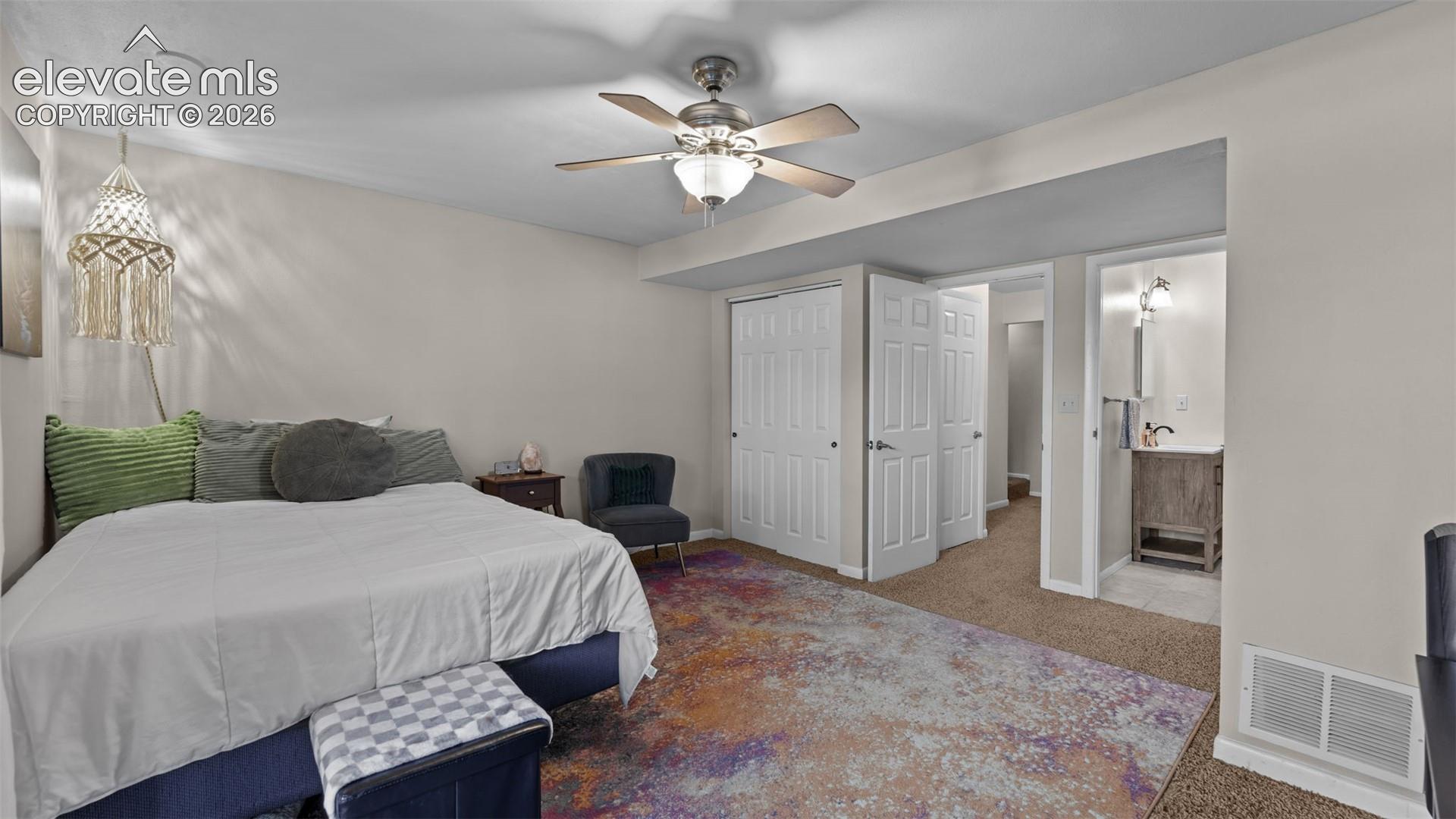 Neutral wall tones, ceiling fan with light fixture, dual-panel closet doors, and attached bathroom featuring a wooden vanity