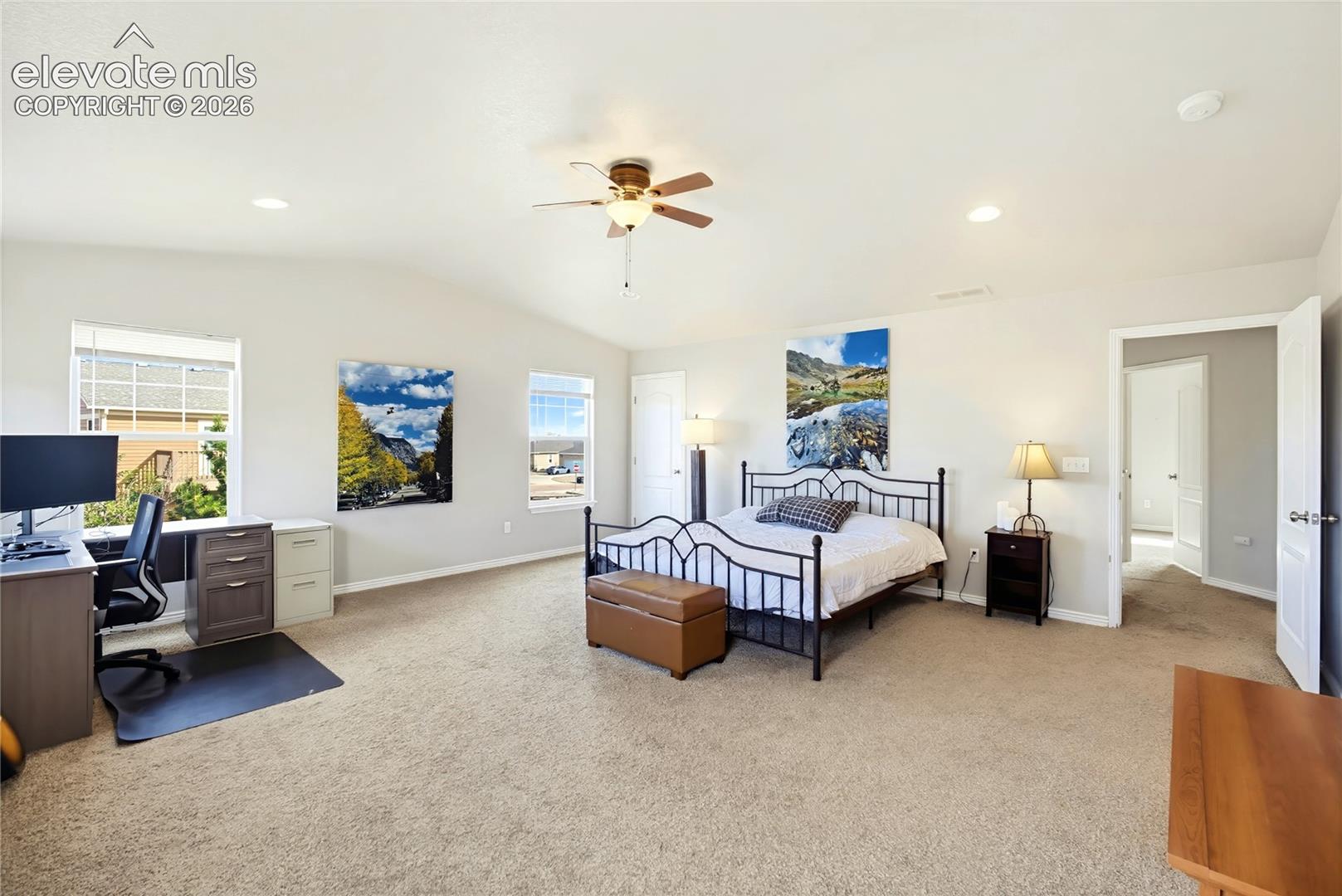 Spacious interior featuring neutral-toned carpeting, vaulted ceilings, a central ceiling fan, and large windows