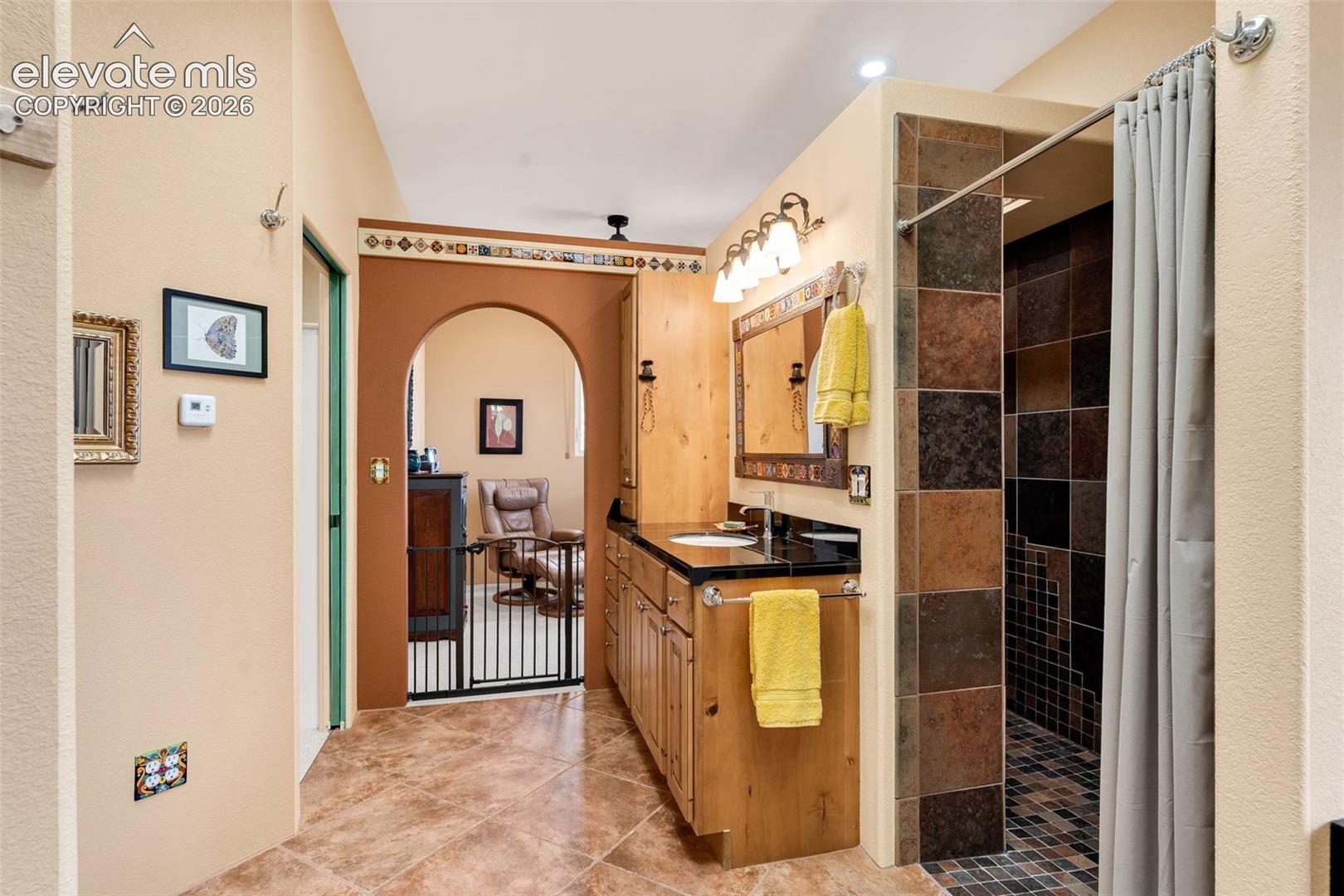 Bathroom featuring stone tile flooring, a custom wood vanity with a stone countertop, an arched entryway, and a walk-in shower with multi-tone stone wall tiles