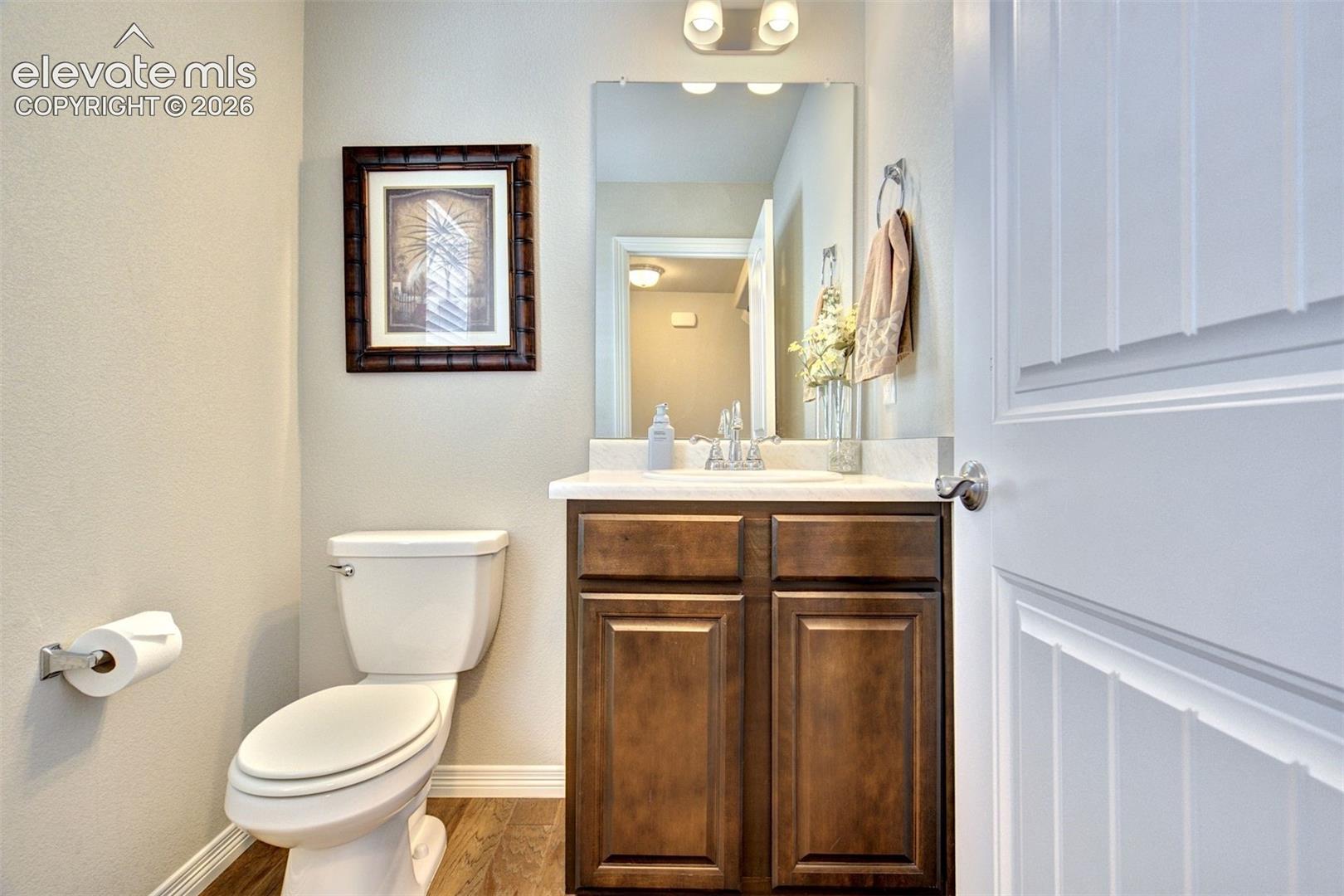 Dark wood-finish vanity with a stone countertop, integrated sink, wall-mounted rectangular mirror, and two-bulb overhead light fixture