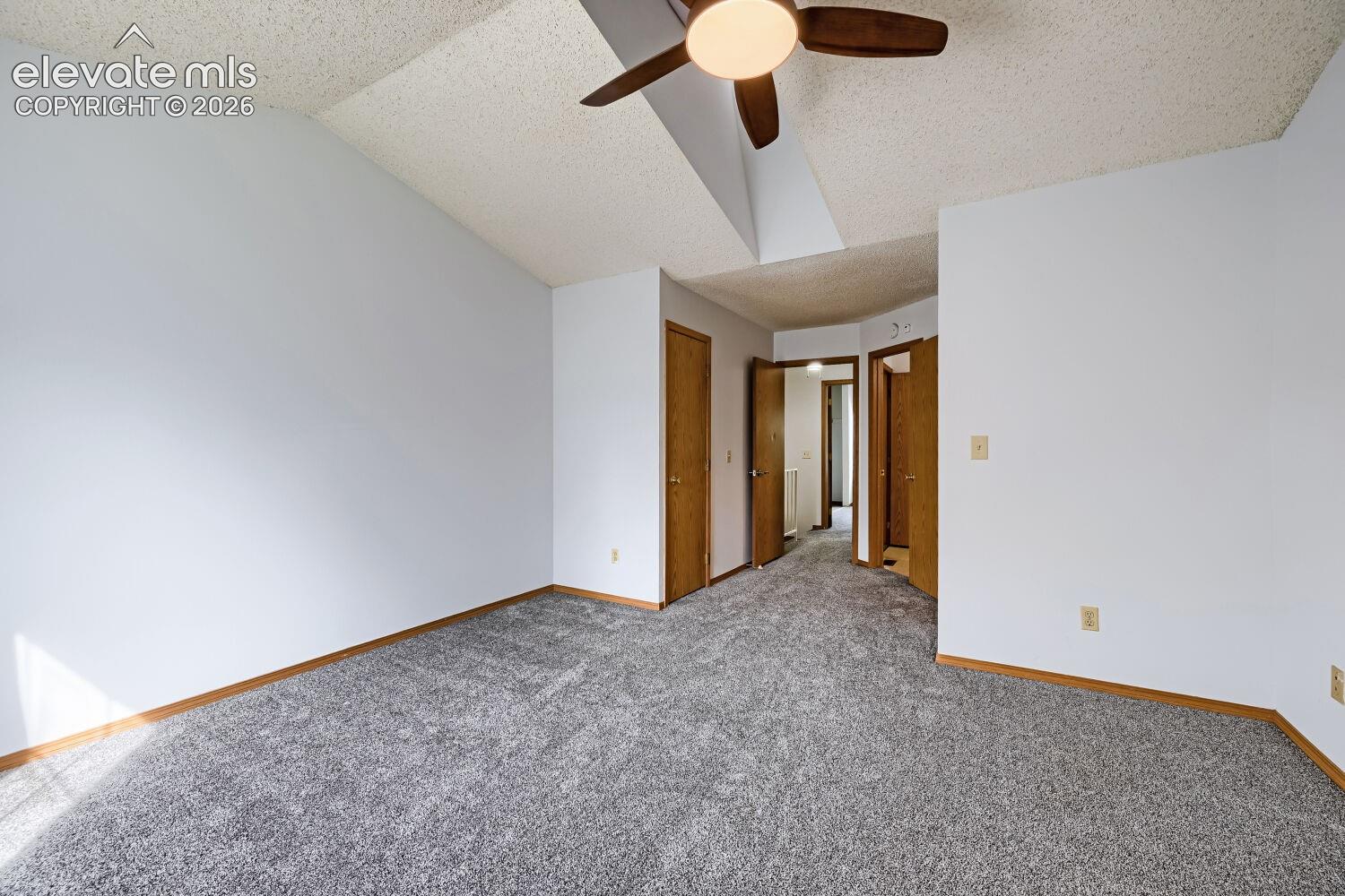 Vaulted ceiling with a ceiling fan, grey carpeting, wood trim, and multiple doorways