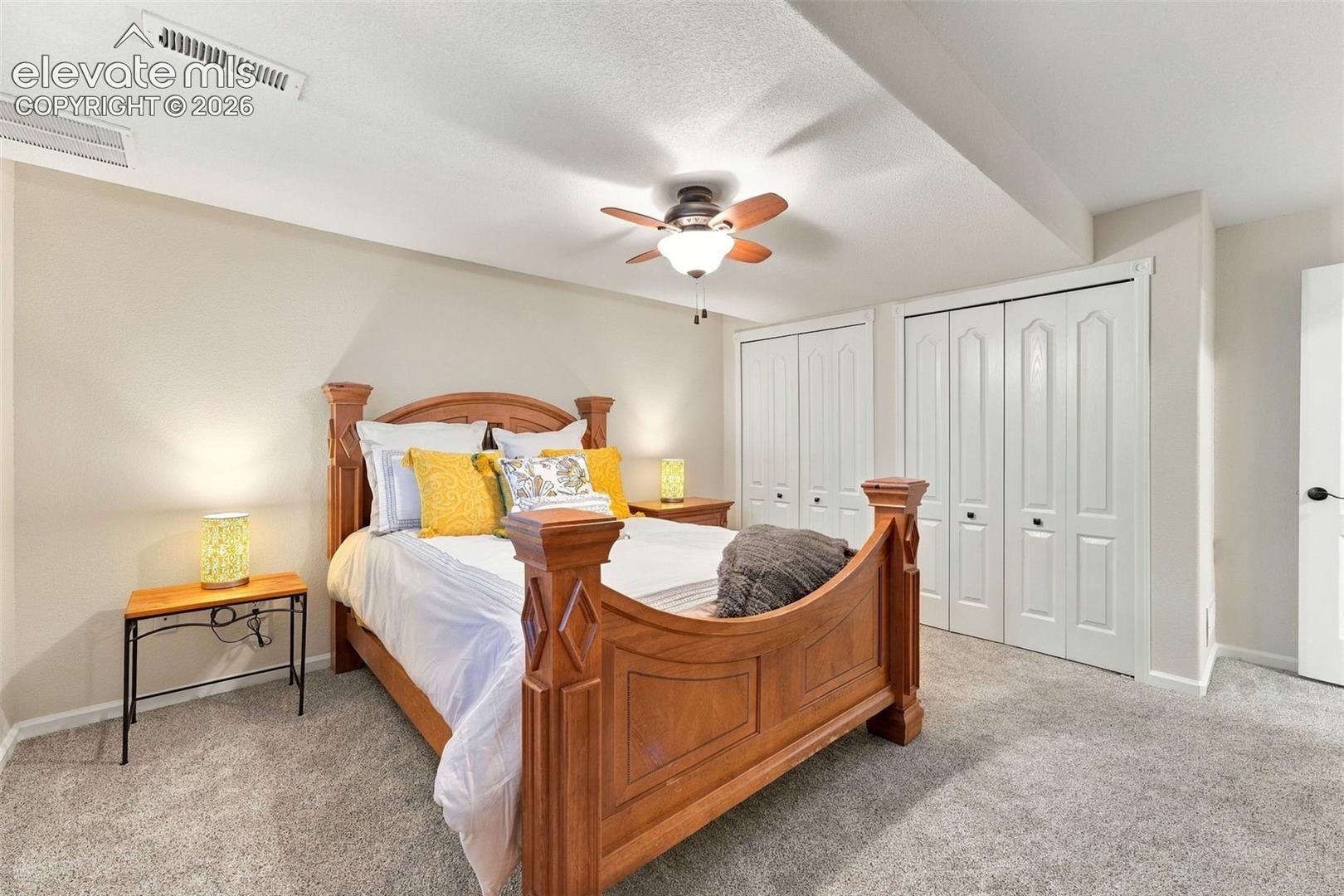 Neutral carpeting, dual bi-fold closets with paneled doors, and a ceiling-mounted light fixture with a fan