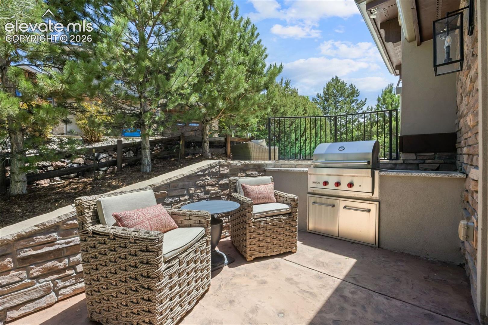 Outdoor patio featuring a built-in stainless steel grill, stone veneer retaining walls, and a black metal railing