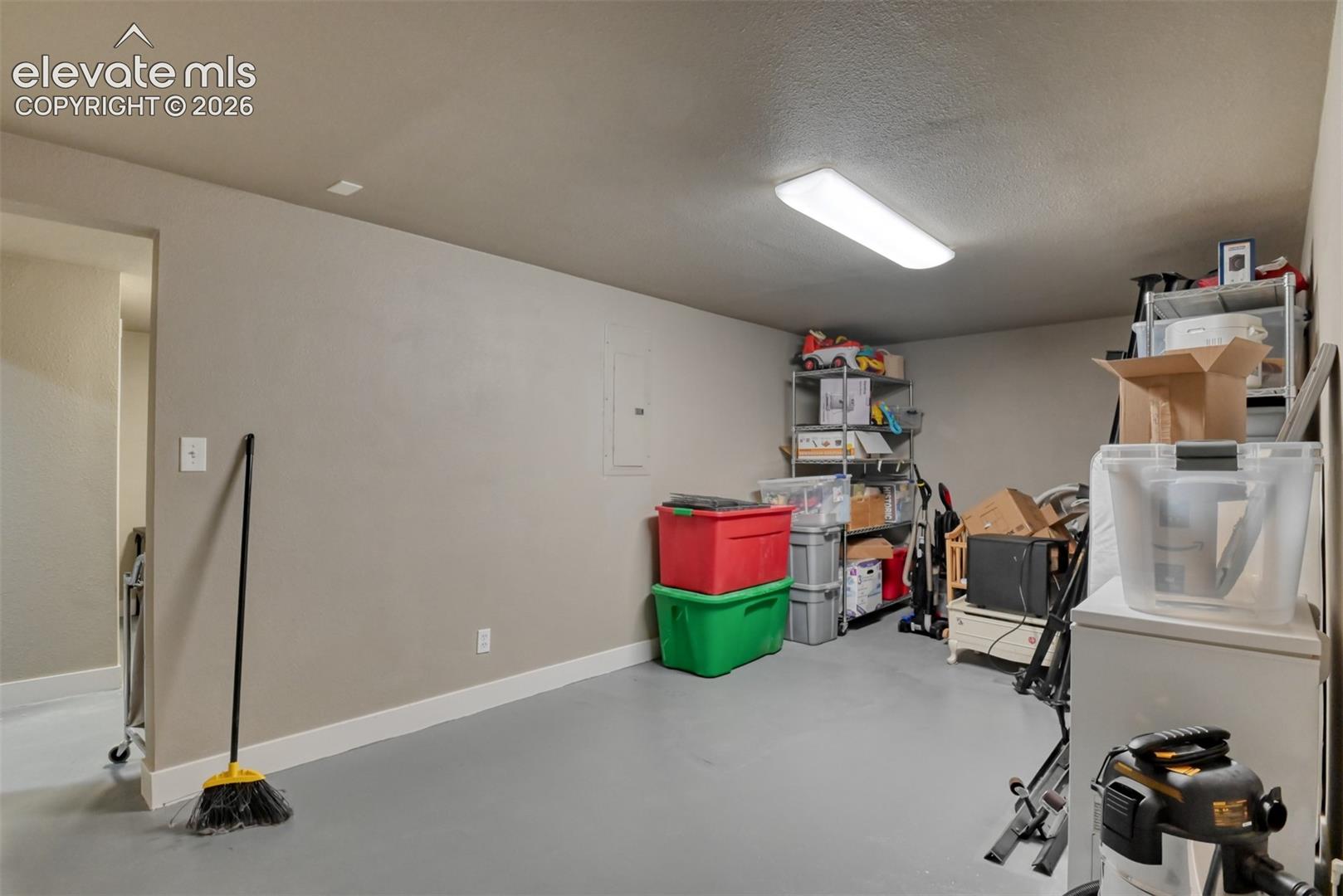 Basement with white fridge, electric panel, and a textured ceiling