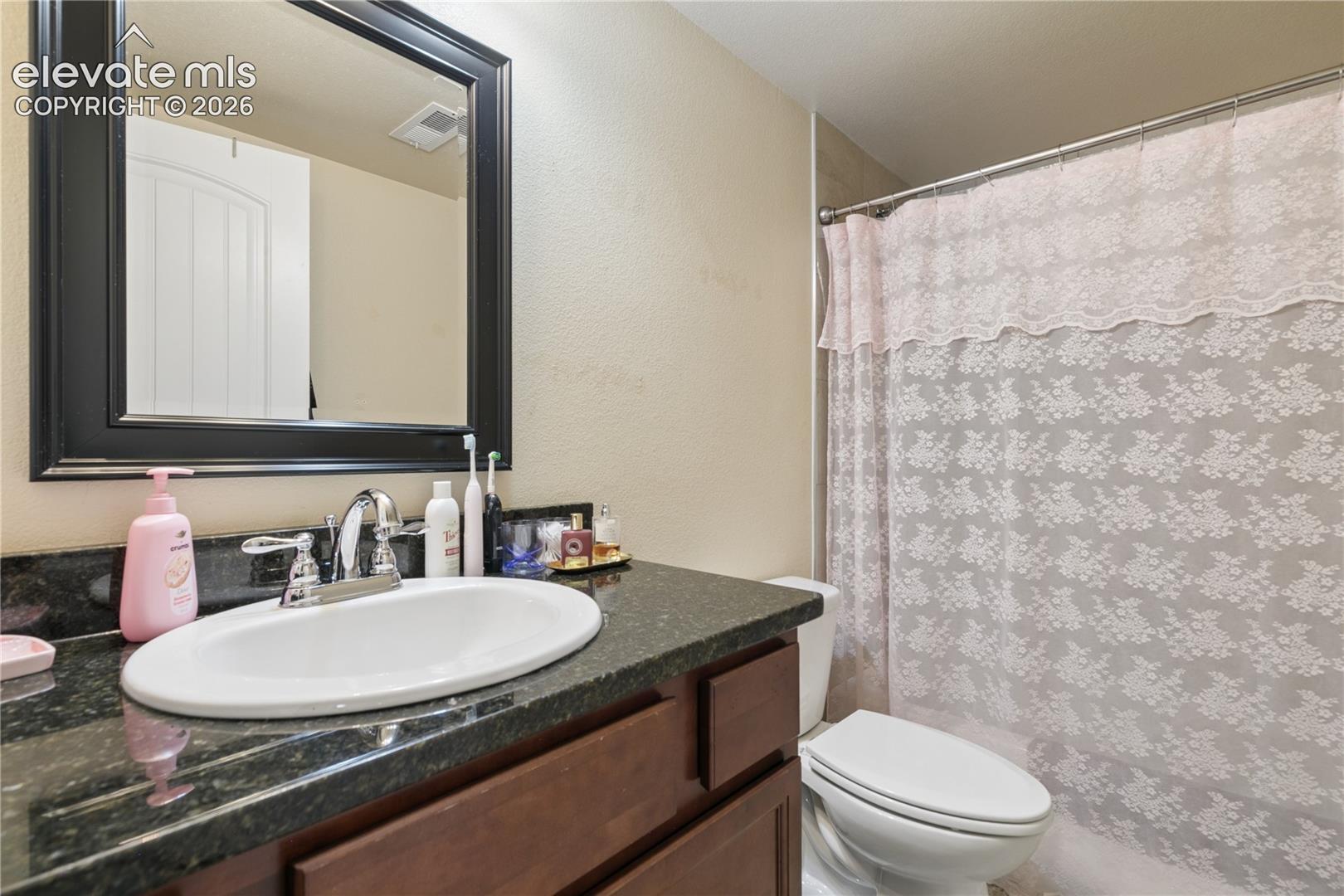 Bathroom featuring a dark wood vanity with a dark speckled countertop, an undermount oval sink with a chrome faucet, and a framed wall mirror