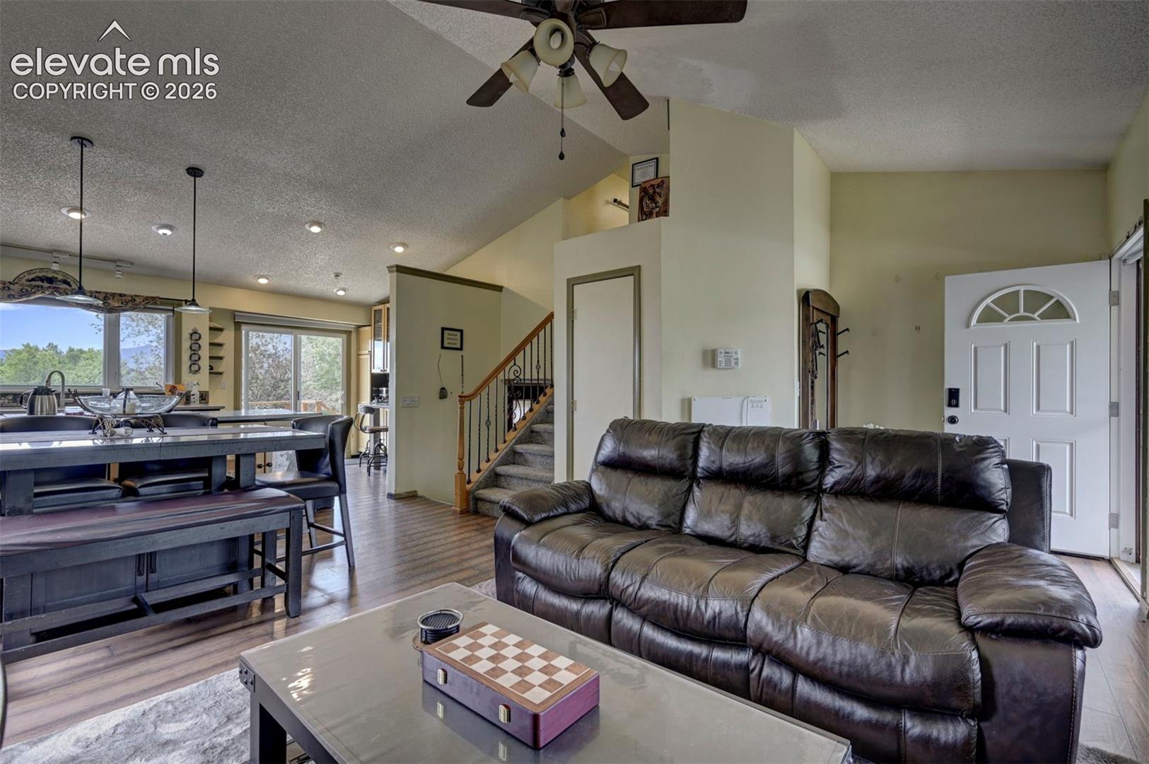 Open-concept living area featuring wood-finish flooring, a vaulted ceiling with a ceiling fan, and a kitchen island with pendant lighting