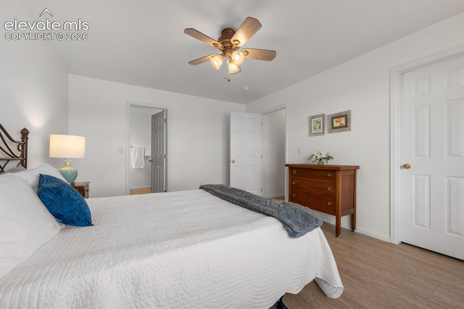 Neutral-toned interior featuring wood-finish flooring, a multi-blade ceiling fan with integrated lighting, and white six-panel interior doors