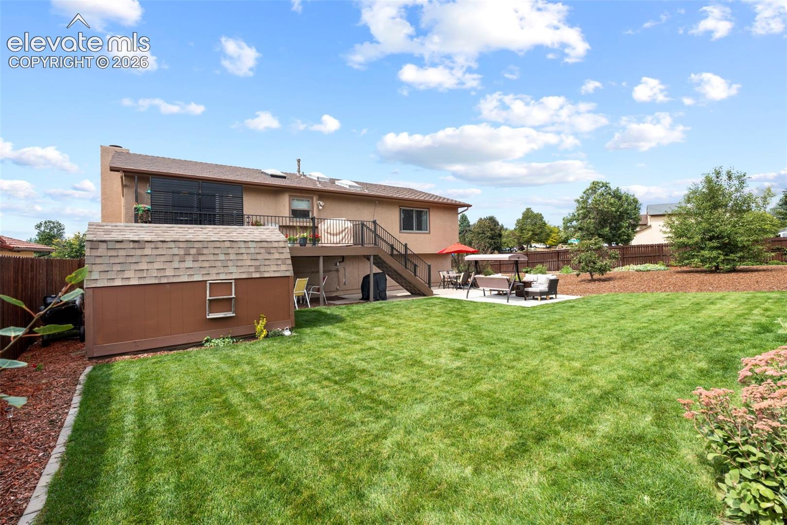Expansive backyard featuring a manicured lawn, a raised wood deck with metal railing, a paved patio area, and a detached storage shed