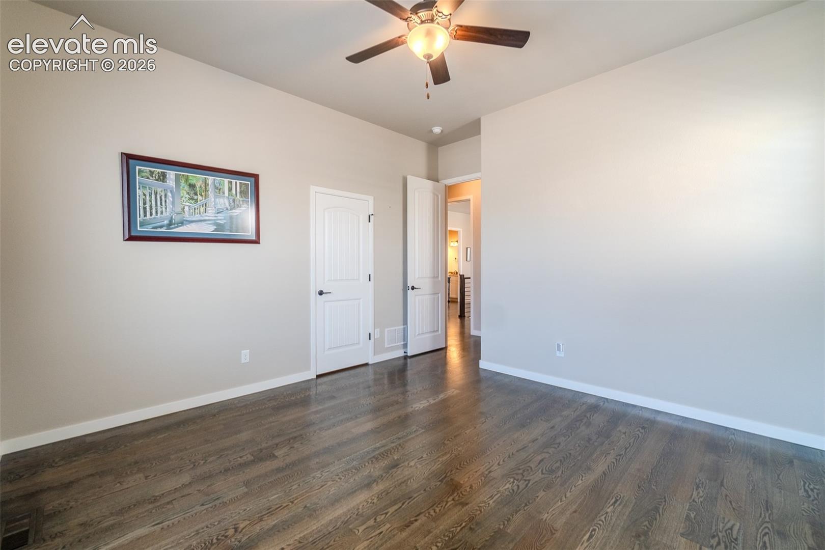 Spacious room featuring wood-finish flooring, two windows with white louvered shutters, a ceiling fan with integrated lighting, and neutral wall paint