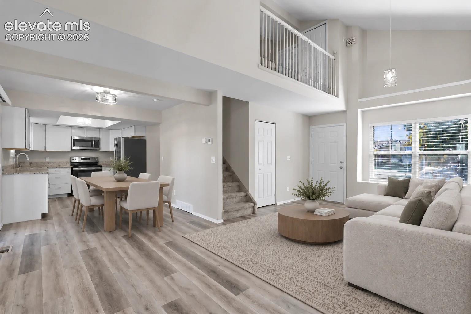 Open floor plan featuring vaulted ceilings, wood-finish flooring, a mezzanine overlook with white railing, and a kitchen equipped with stone-surface countertops and stainless steel appliances