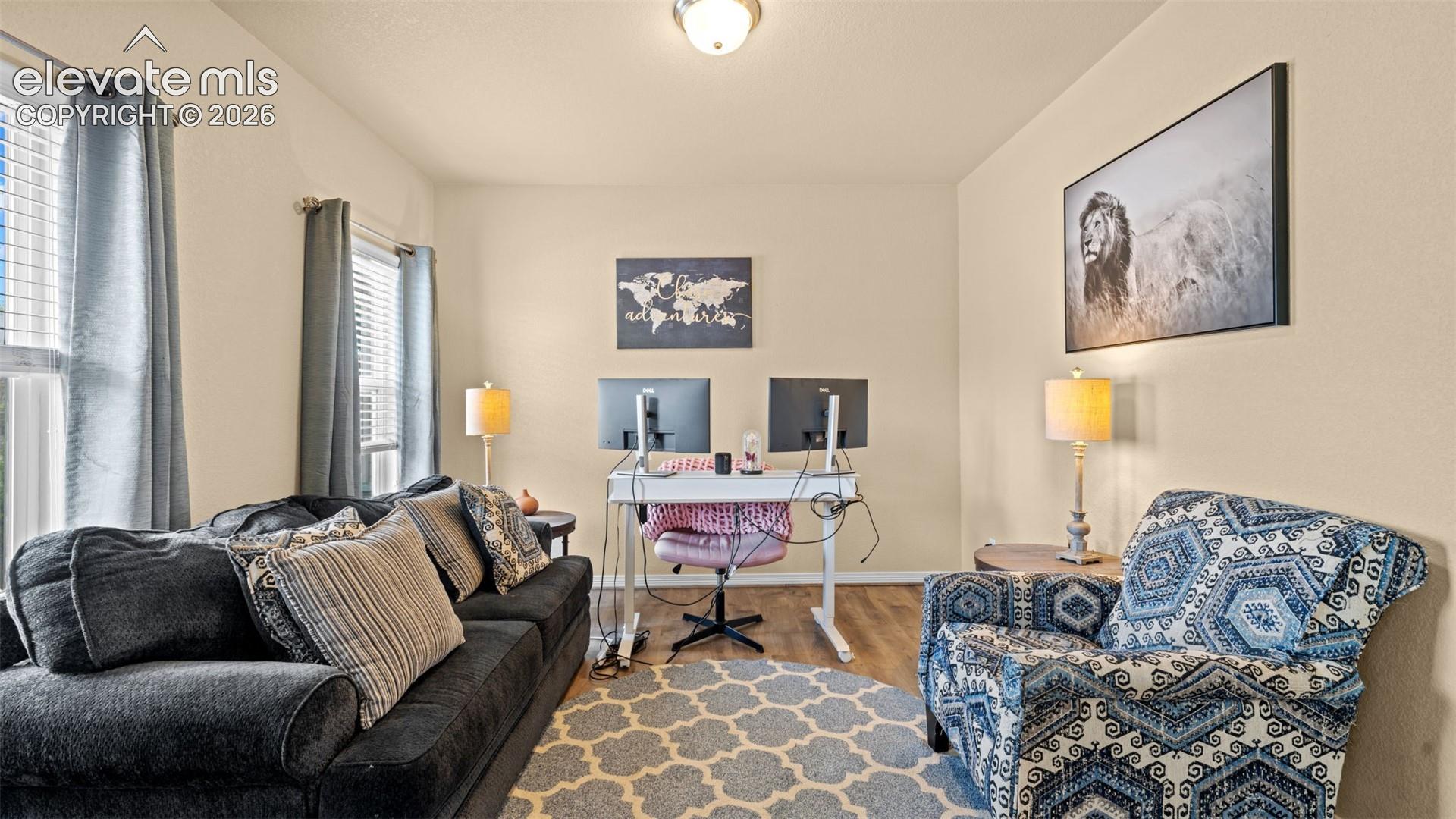 Versatile room featuring light-toned walls, wood-finish flooring, and multiple windows with blinds