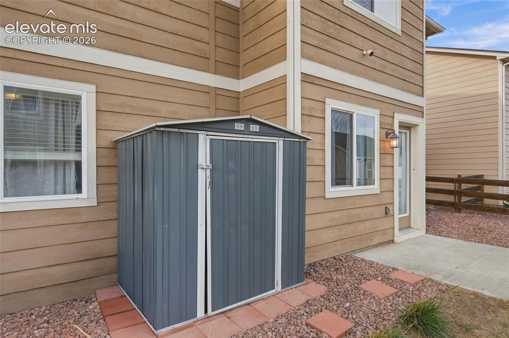 Exterior horizontal lap siding with a metal storage shed, concrete entry pad, and wall-mounted exterior light fixture