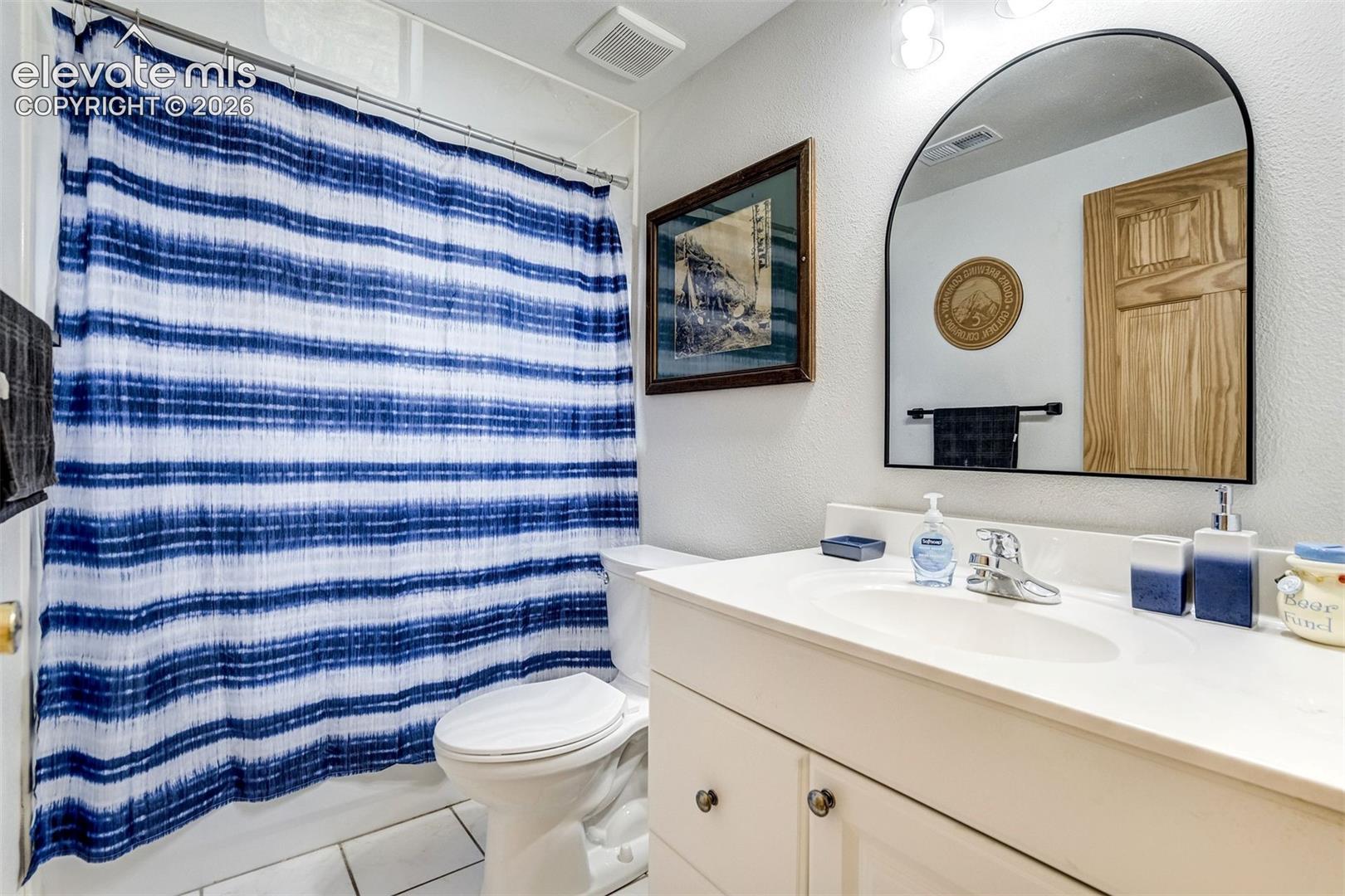 Full bathroom featuring a white vanity with integrated sink, chrome faucet, and an arched mirror with a black frame
