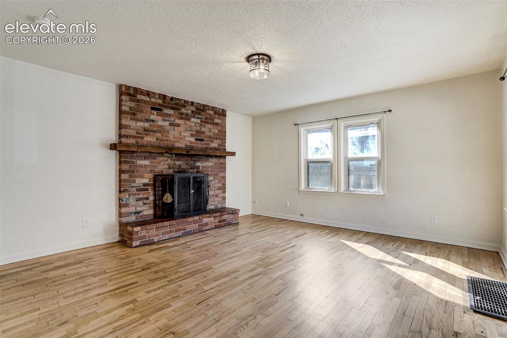 Full-height brick fireplace with a wood mantel, wood-finish flooring, and two double-hung windows