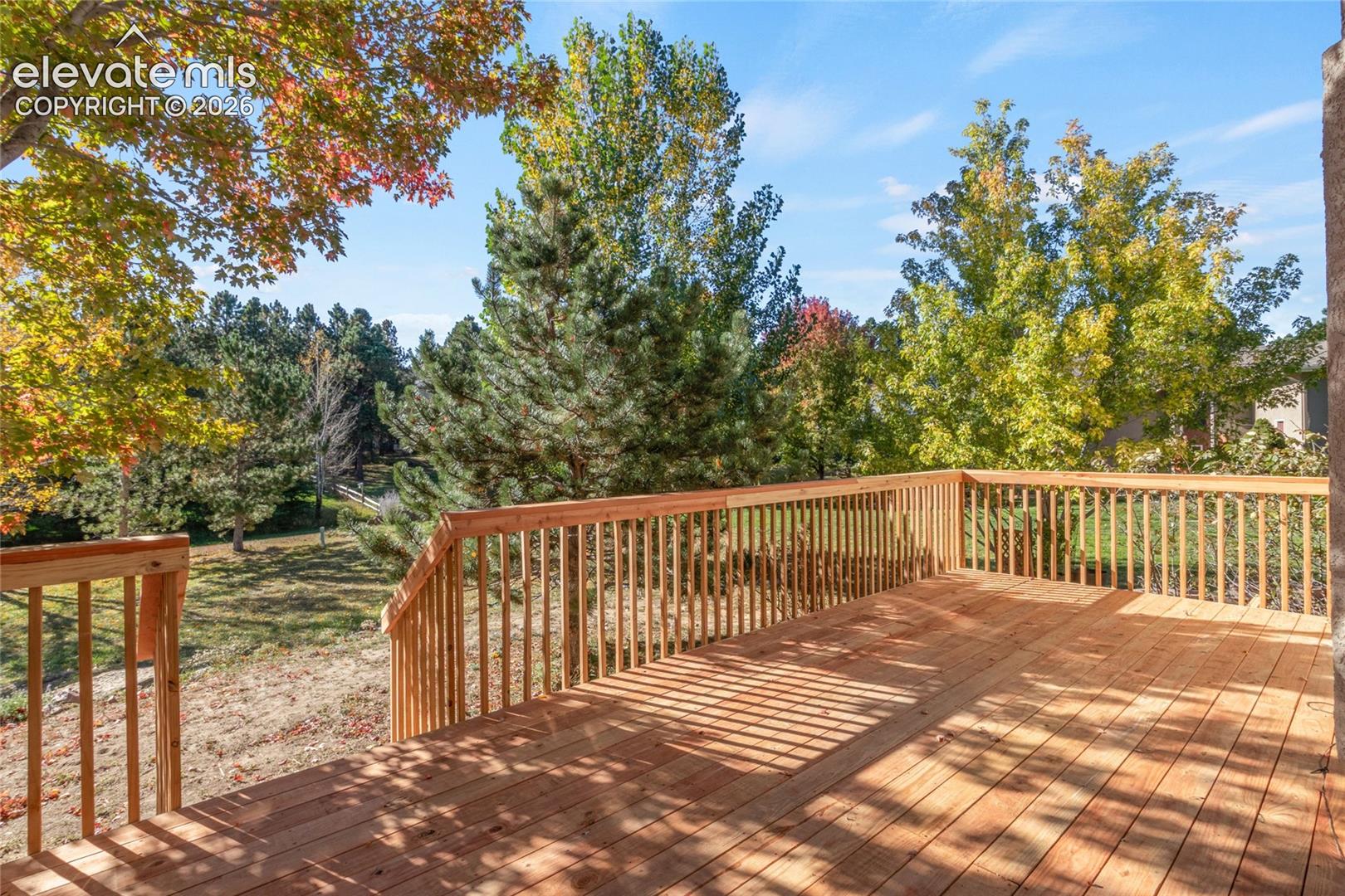 Elevated wooden deck with vertical baluster railings and mature trees