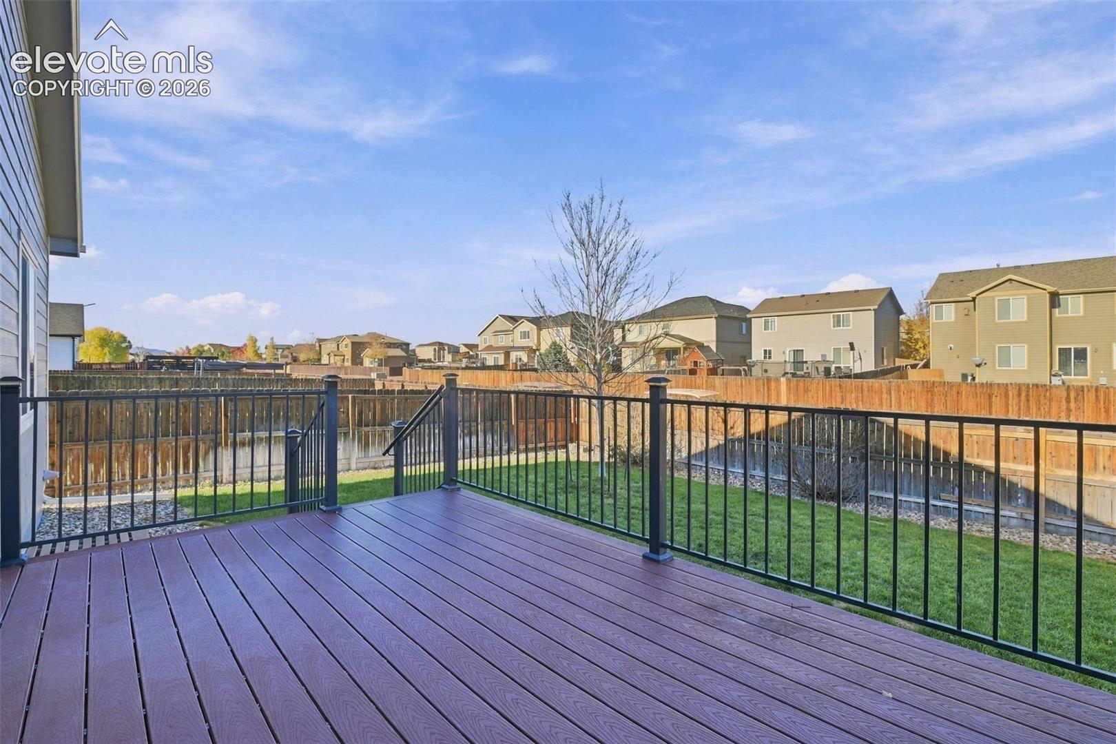 Elevated rear deck featuring composite decking, black metal railing, and staircase access to a fenced yard with lawn space