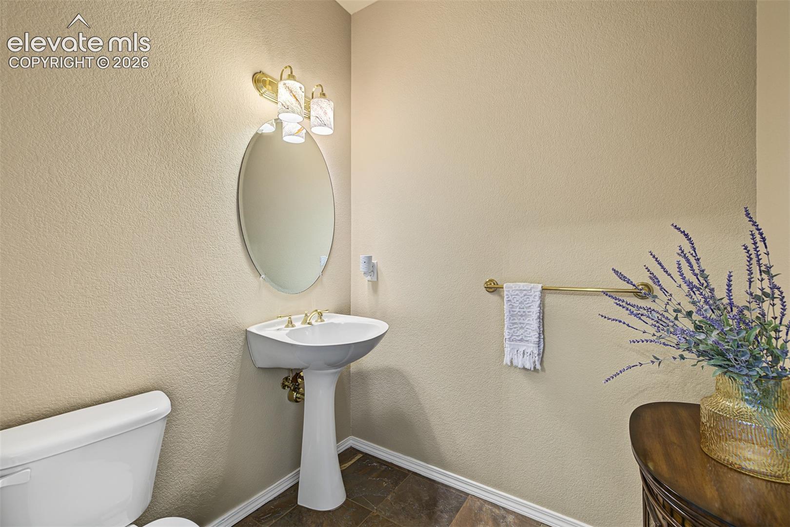 Main-level powder room featuring a pedestal sink, oval mirror, decorative lighting, and tile flooring.