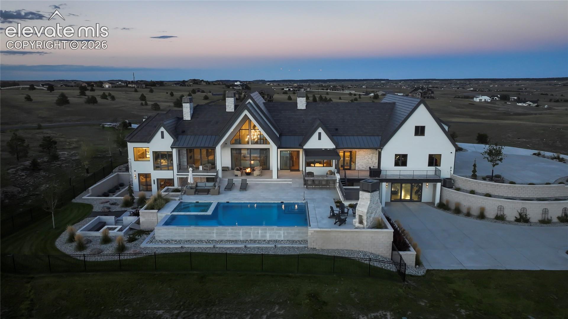Multi-level exterior featuring a stone and siding facade, an infinity-edge swimming pool with integrated spa, multiple stone-surround fire pits, an elevated stone fireplace, and extensive multi-tier concrete patios