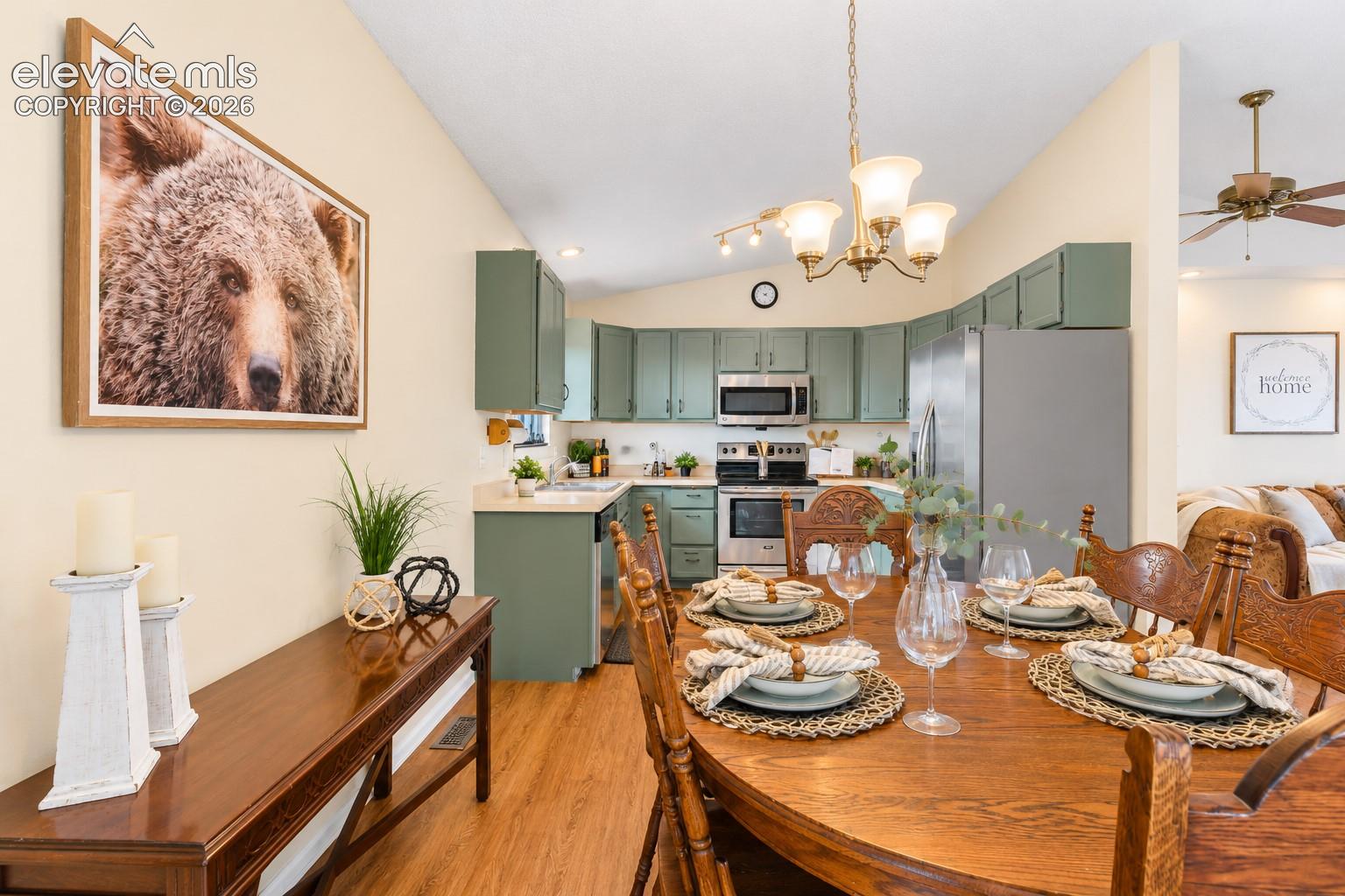 Kitchen featuring sage green cabinetry, stainless steel appliances, and wood-finish flooring, illuminated by a multi-bulb chandelier