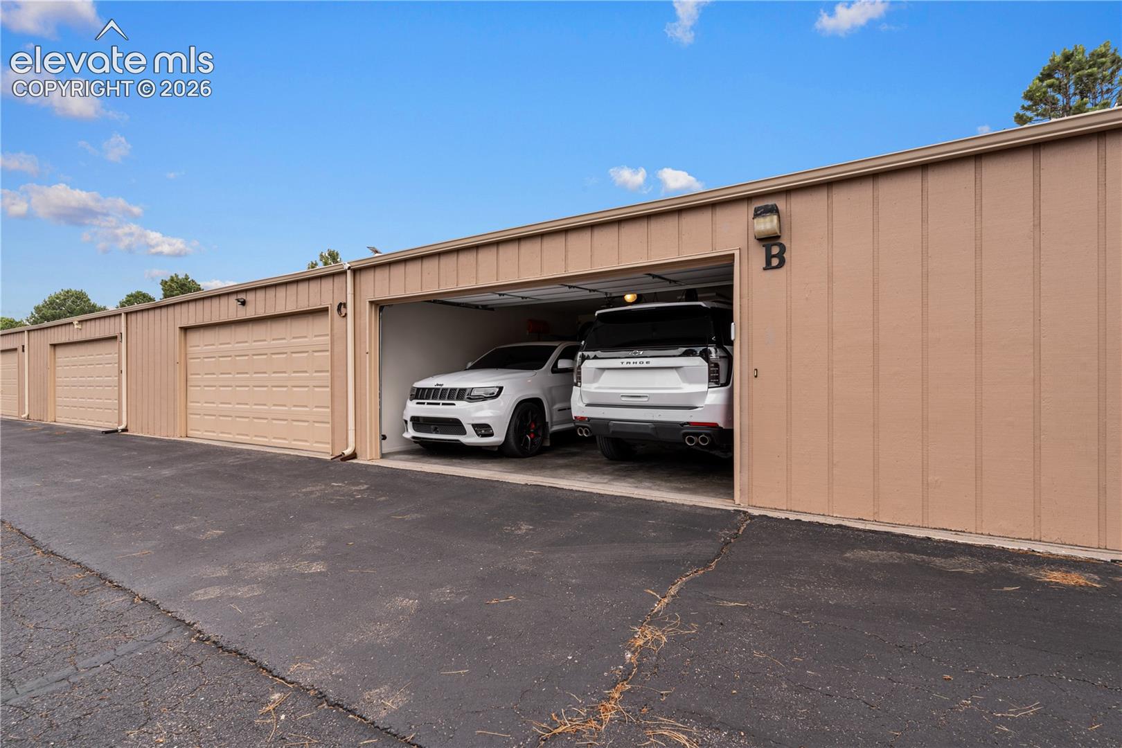 Detached metal-siding garage structure featuring multiple individual bays, overhead roll-up doors, asphalt apron, and wall-mounted exterior lighting