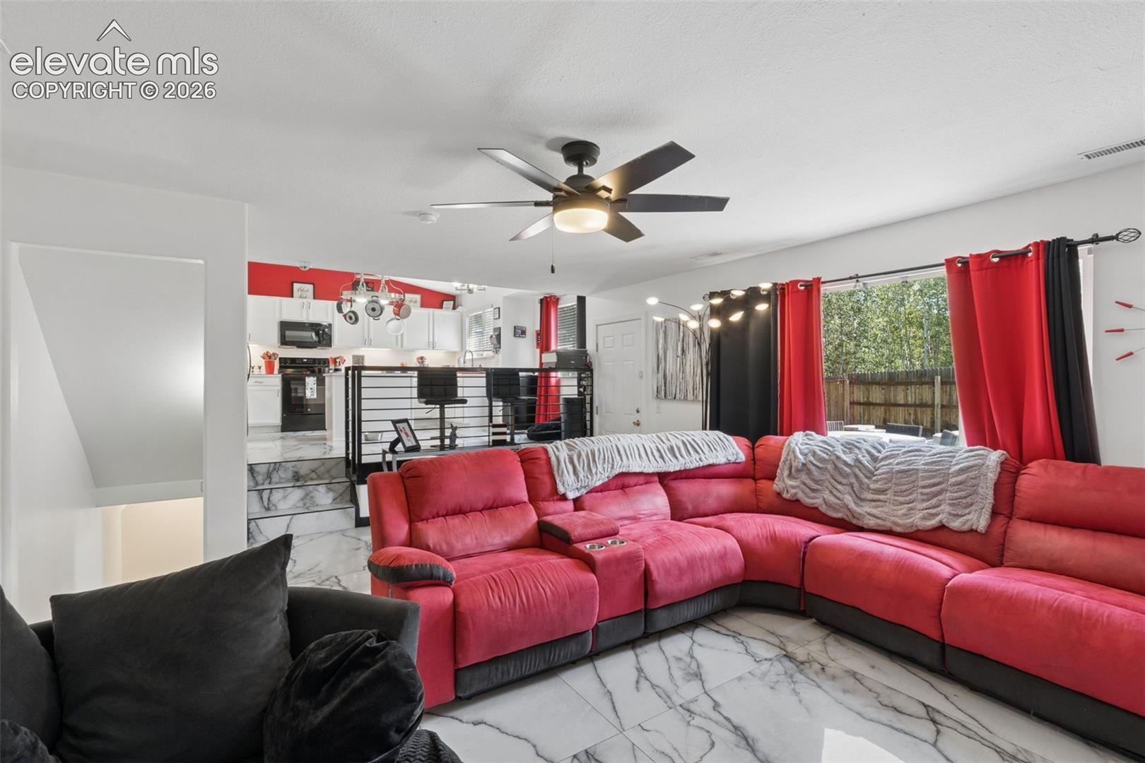 Glossy tile flooring, white cabinetry, a kitchen island with seating, a ceiling fan, and a glass sliding door