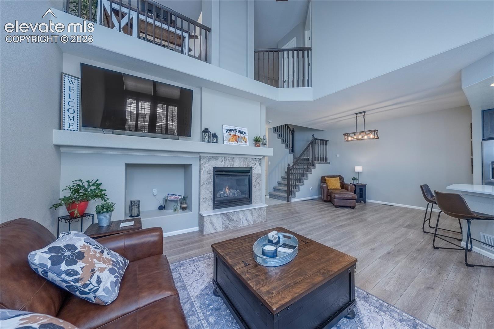 Two-story vaulted ceiling with loft overlook, floor-to-ceiling stone-tiled fireplace, wood-finish flooring, and built-in recessed wall shelving