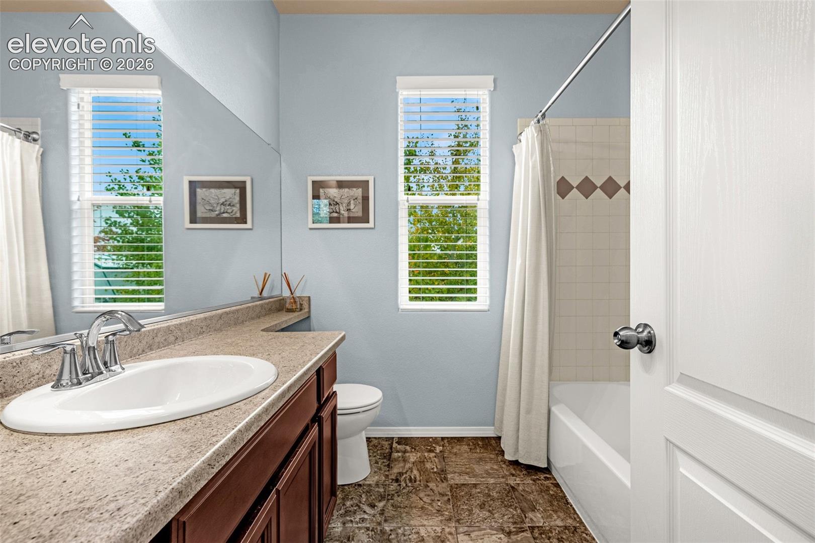 Bathroom featuring an oval drop-in sink, stone-surface countertop, dark wood-finish cabinetry, tile flooring, and a tub-shower combination with decorative accent tile