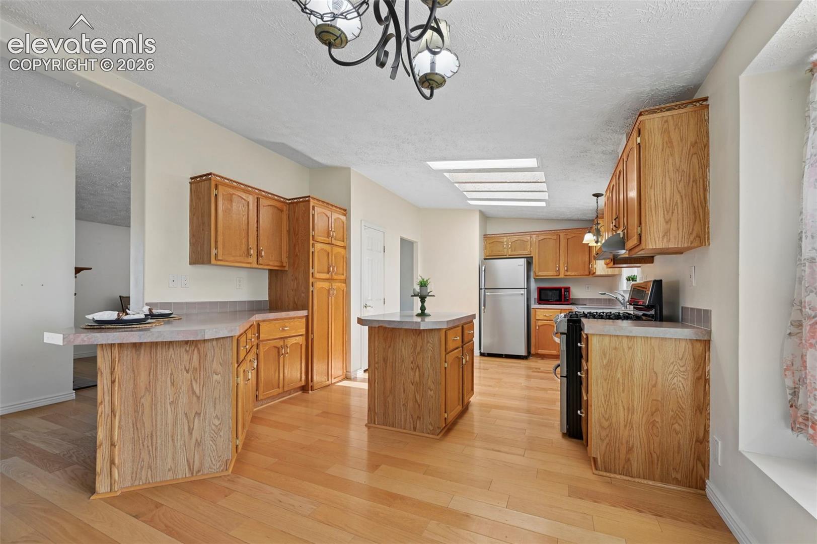 Kitchen featuring wood-finish flooring, wood cabinetry, a center island, stainless steel refrigerator, and a ceiling skylight