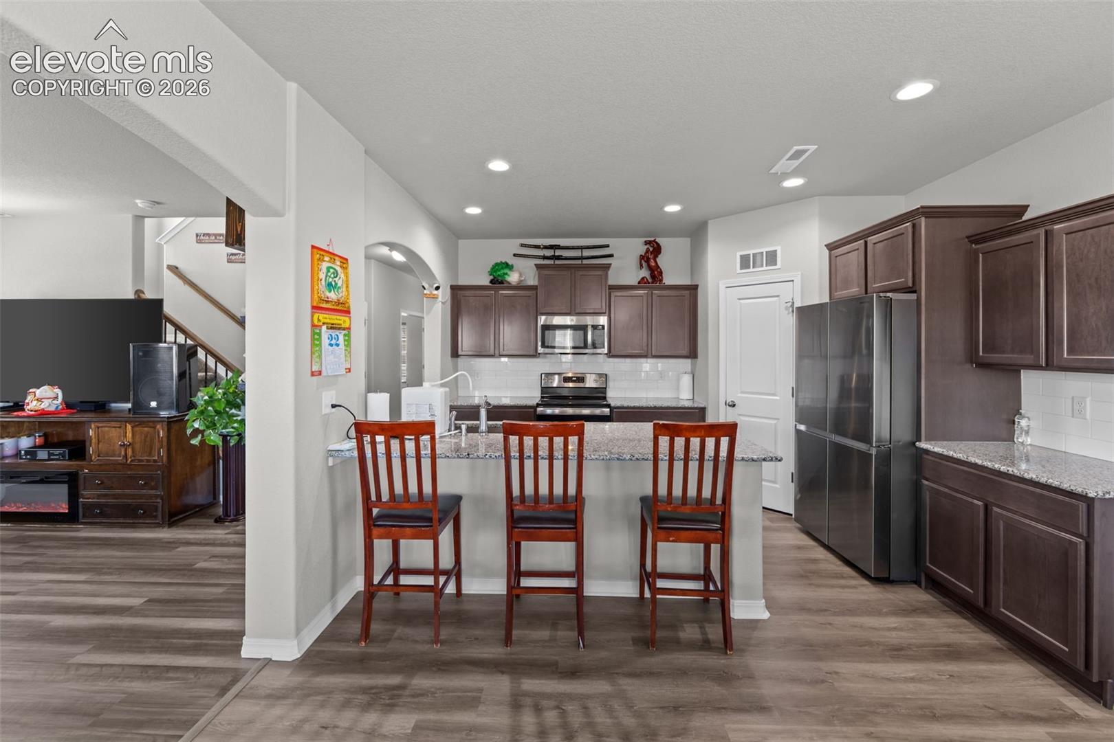 Kitchen featuring wood-finish flooring, dark wood cabinetry, stainless steel appliances, a white tile backsplash, and light-toned countertops