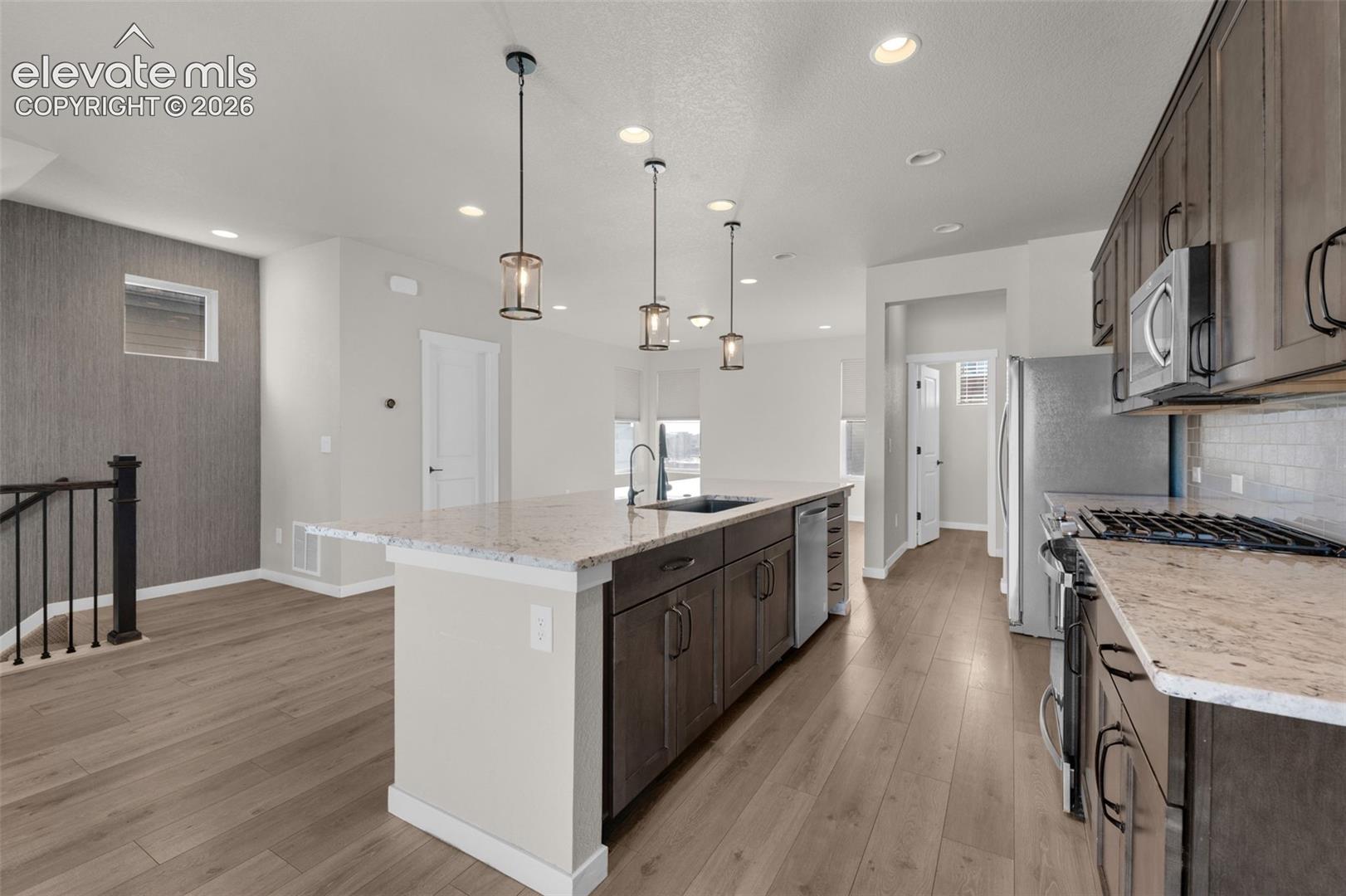 Spacious kitchen featuring a large island, wood-finish flooring, recessed lighting, pendant lighting, and stainless steel appliances