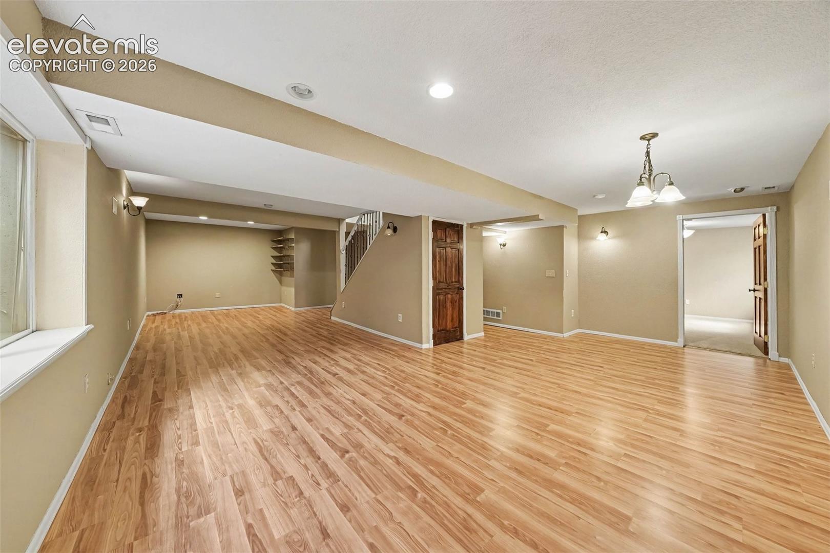 Expansive room featuring wood-finish flooring, recessed lighting, wall sconces, a staircase, and a built-in shelving unit