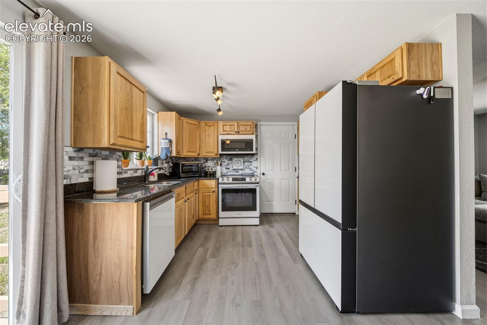 Wood-finish cabinetry with dark countertops, tile backsplash, and light wood-finish flooring