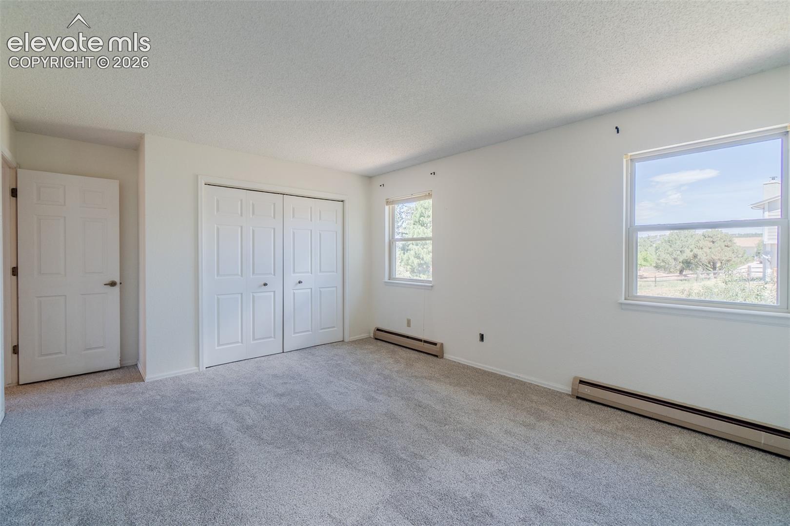 One of Four Spacious upstairs bedroom featuring light gray new carpet, neutral wall paint, two windows, and a bi-fold closet