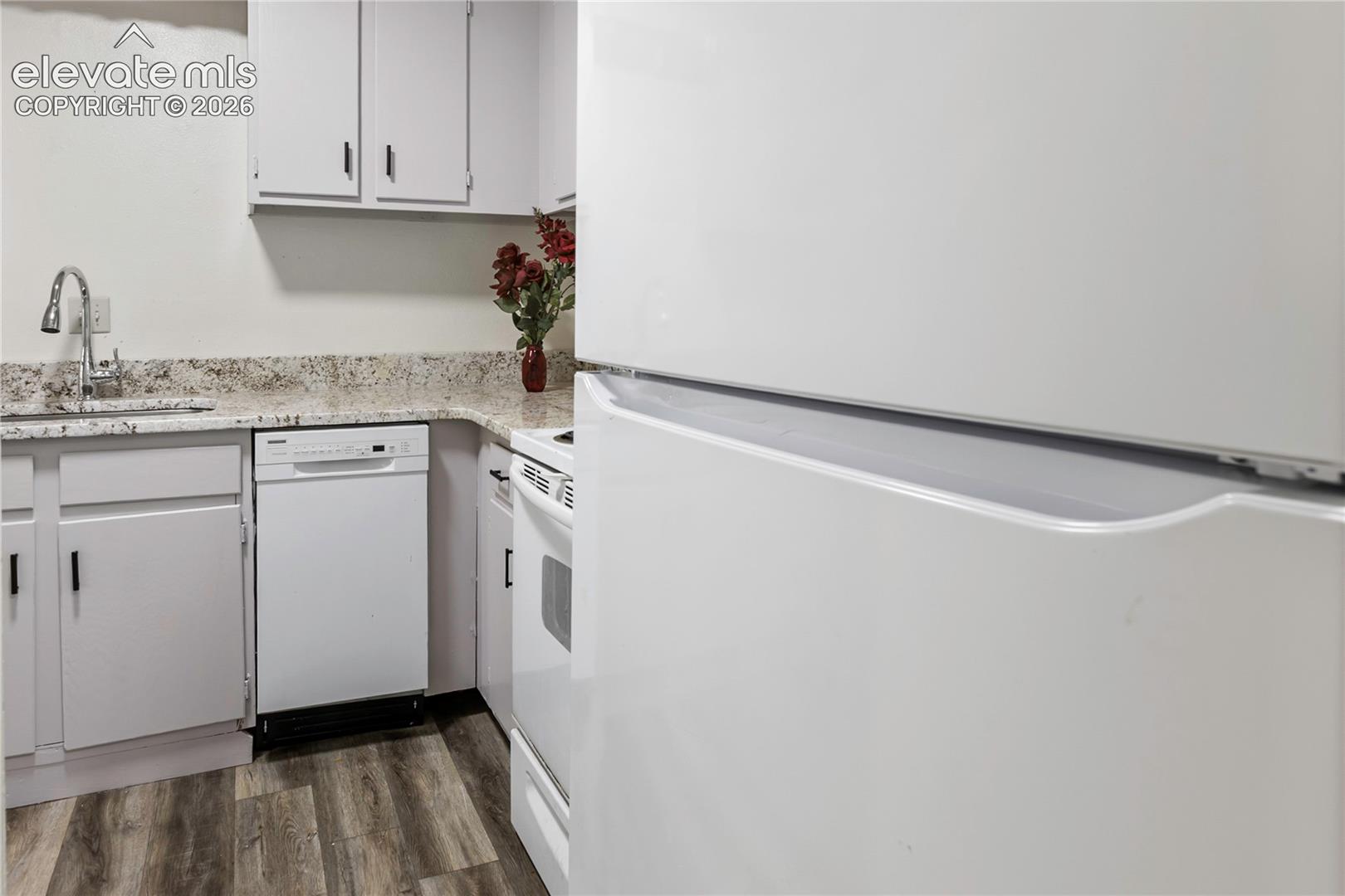 Kitchen featuring white cabinetry, speckled countertops, a gooseneck faucet, a built-in dishwasher, and wood-finish flooring