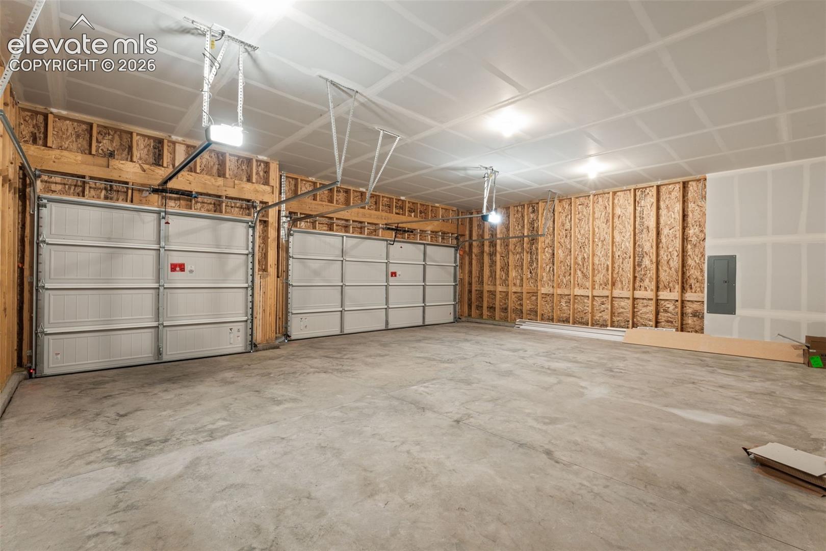 Two white garage doors with automatic openers, exposed wood framing, and a concrete floor