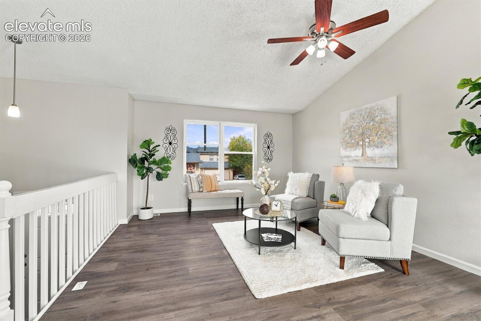 Vaulted ceilings with a multi-blade ceiling fan, wood-finish flooring, and white spindle railing