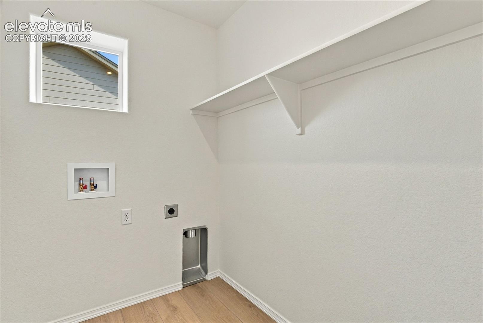 Utility room featuring wood-finish flooring, a single window, and a wall-mounted shelf