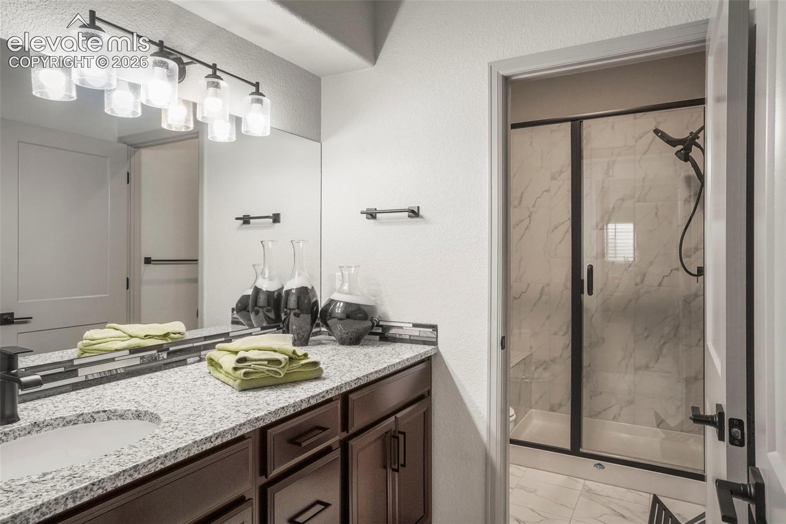Bathroom featuring a dual vanity with granite-finish countertops, dark wood-finish cabinetry, and a full-width mirror